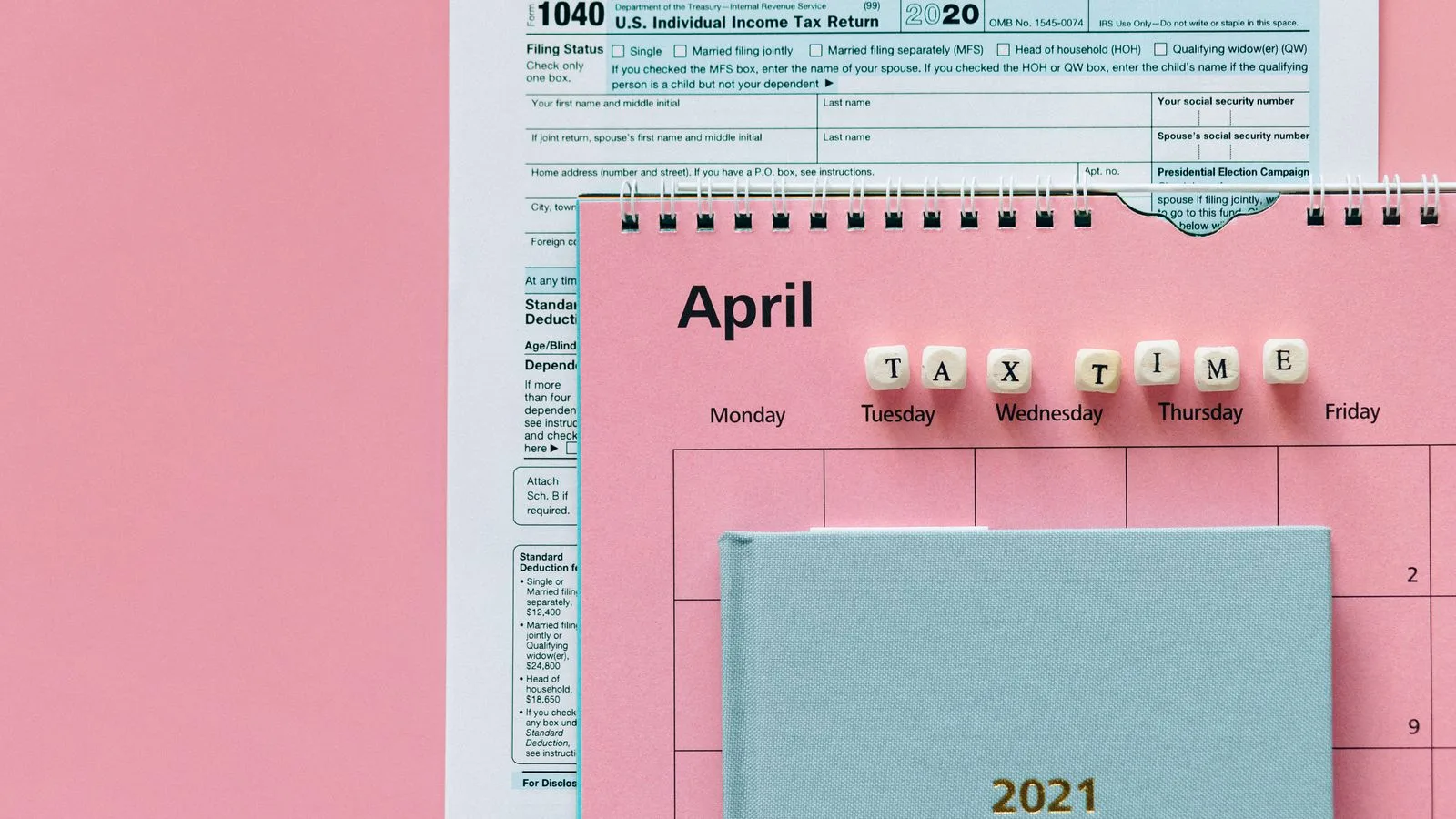 Flat lay image of tax forms, calendar, and 'tax time' reminder on a pink background.