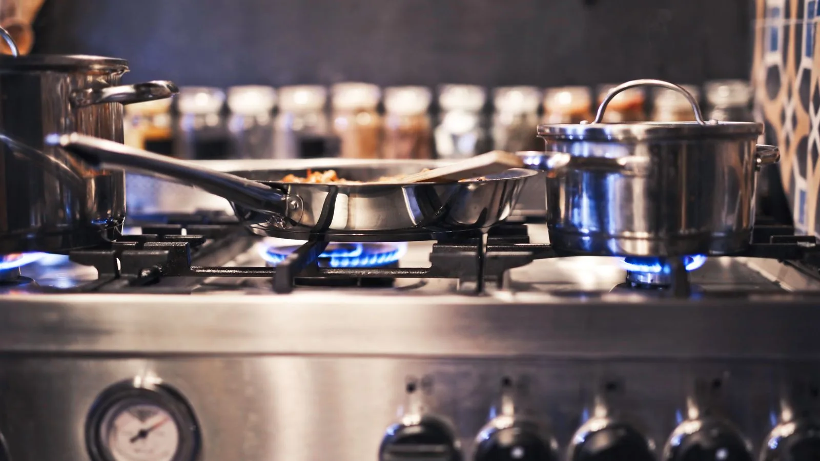 Cooking utensils including pots and pans on a gas stove with blue flames.