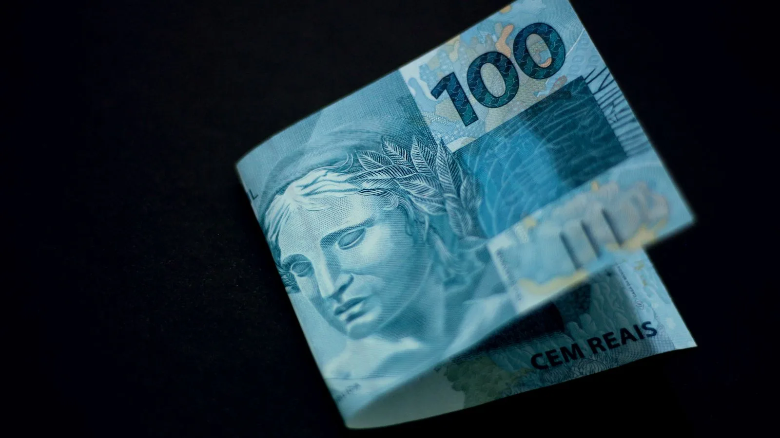 A Brazilian 100 real banknote displayed against a black backdrop, highlighting its design and color.