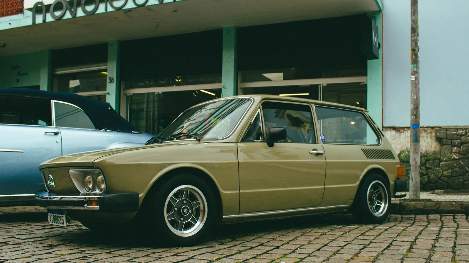A classic vintage car parked in front of a store on a cobblestone street, showcasing urban retro vibes.