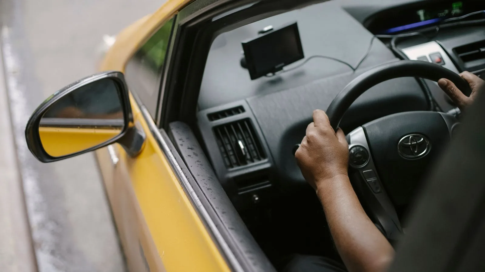 From above of crop unrecognizable person driving modern yellow taxi car with GPS navigator on city street in daytime