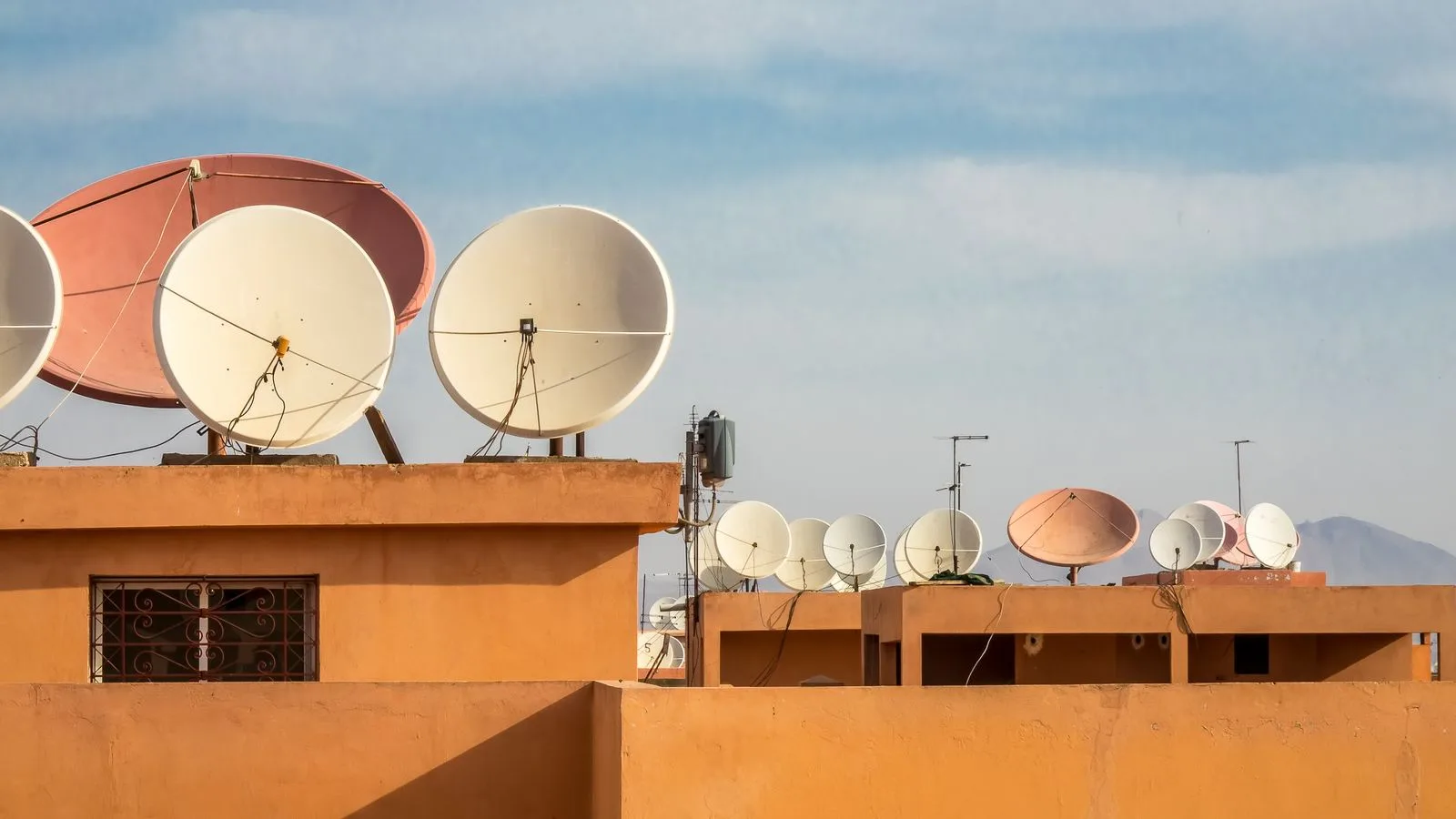 Multiple satellite dishes on orange rooftops under a clear blue sky, capturing urban connectivity.