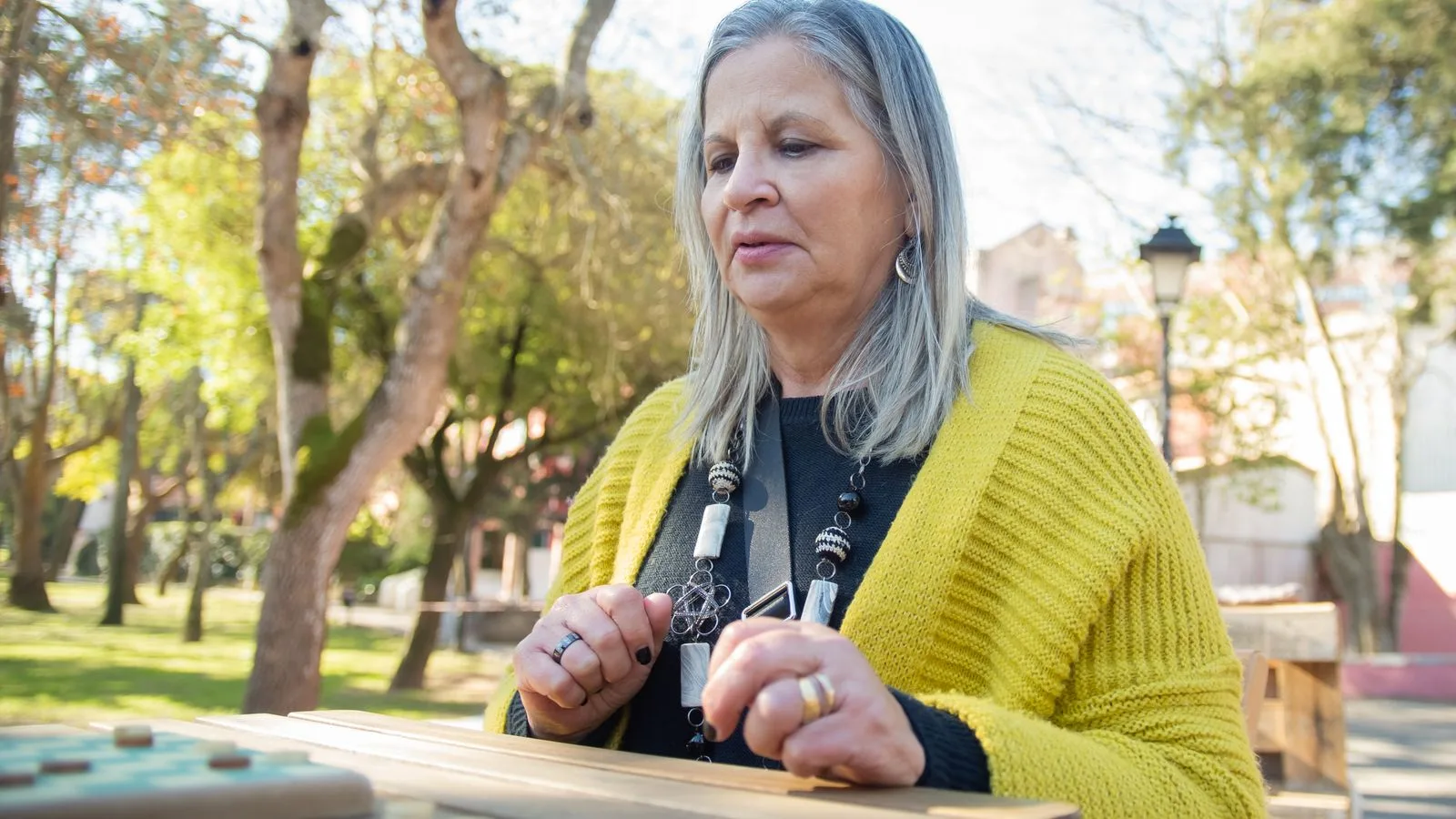 Elderly woman playing a game outdoors, enjoying a sunny day in a Portuguese park.