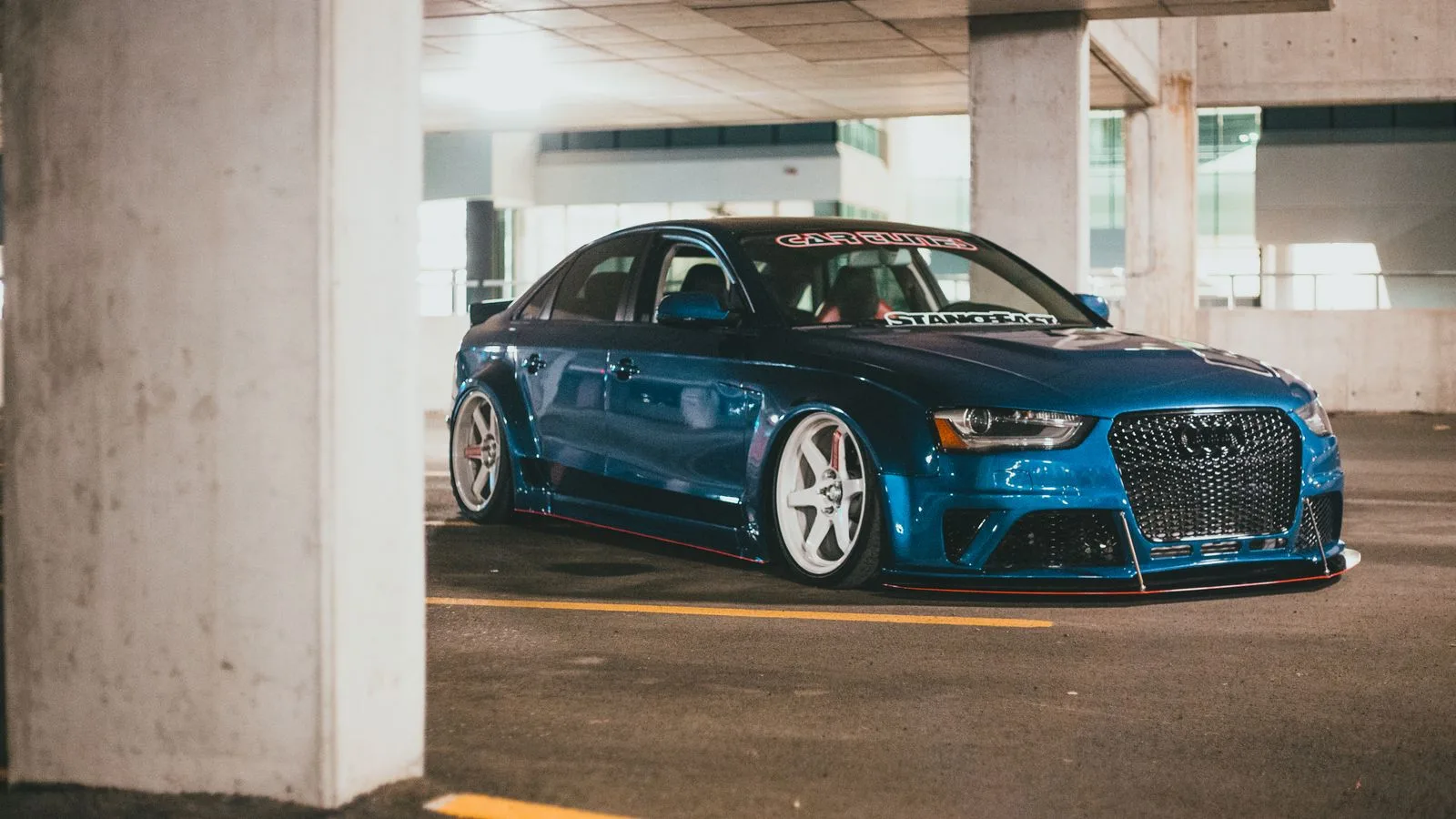 Lowered blue Audi with white rims in an underground parking garage at night.