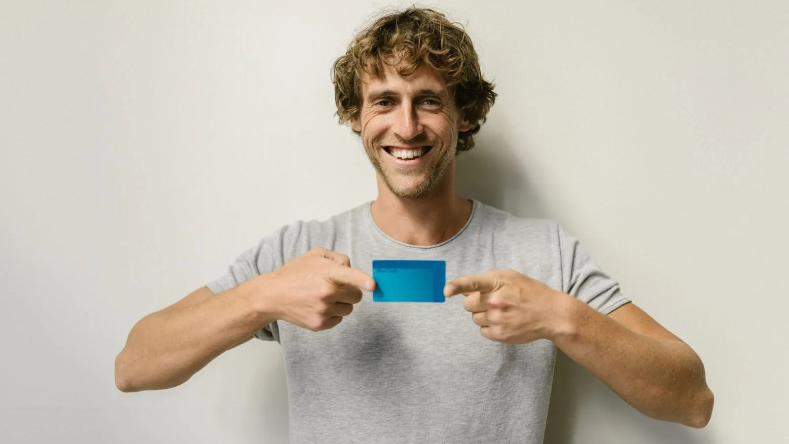 Cheerful man holding a blue credit card against a plain white background.
