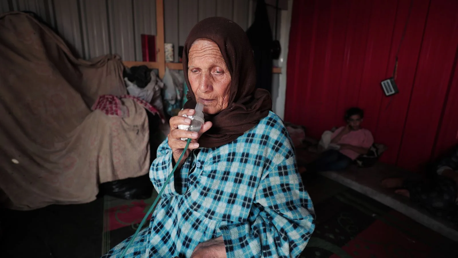 An elderly Middle Eastern woman using an inhaler inside a modest home. Emotionally evocative scene.
