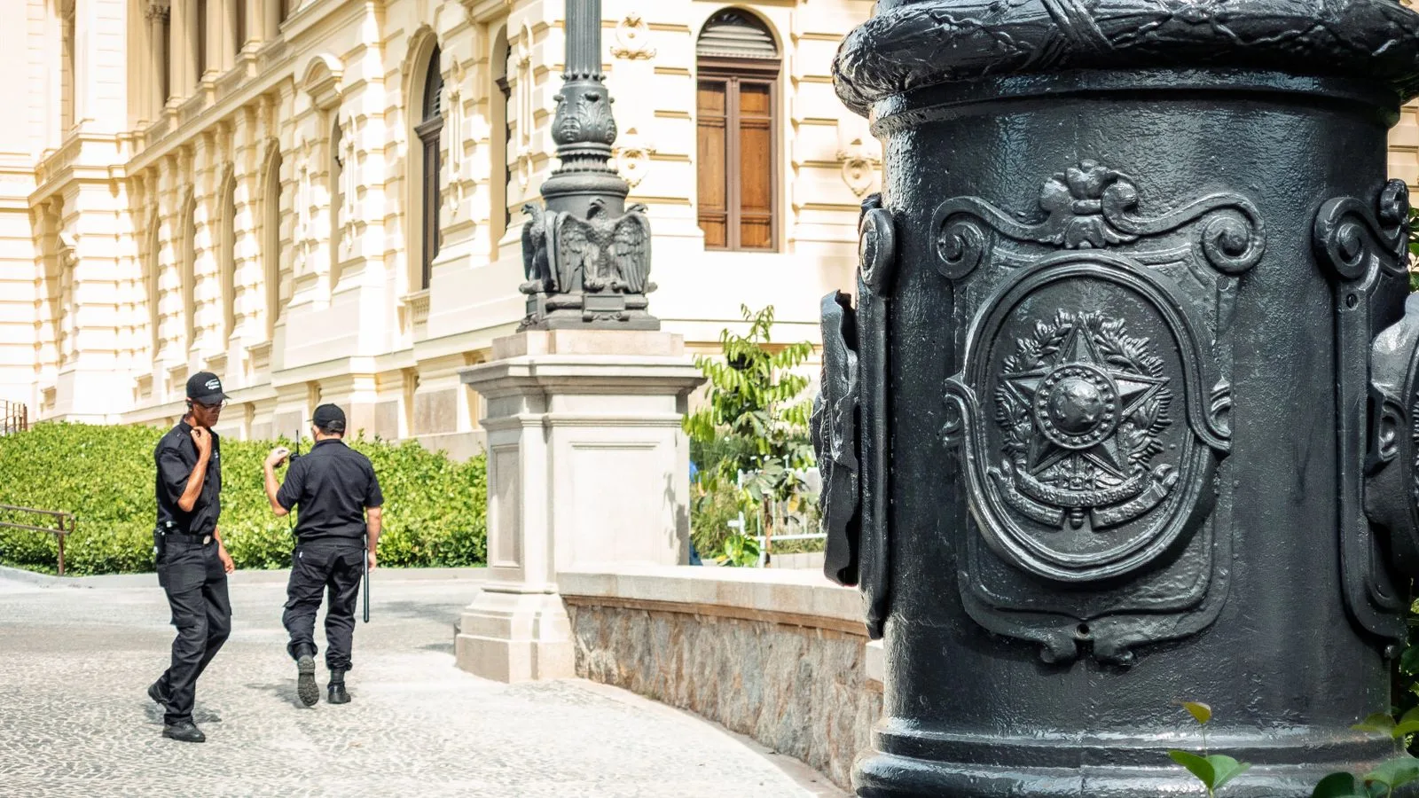 Two security guards patrol in front of ornate historic architecture in São Paulo, Brazil.