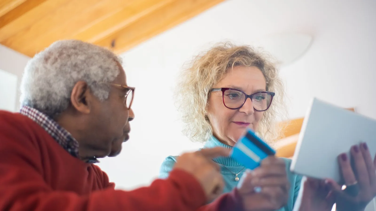 Senior adults using a tablet and credit card for online shopping indoors.