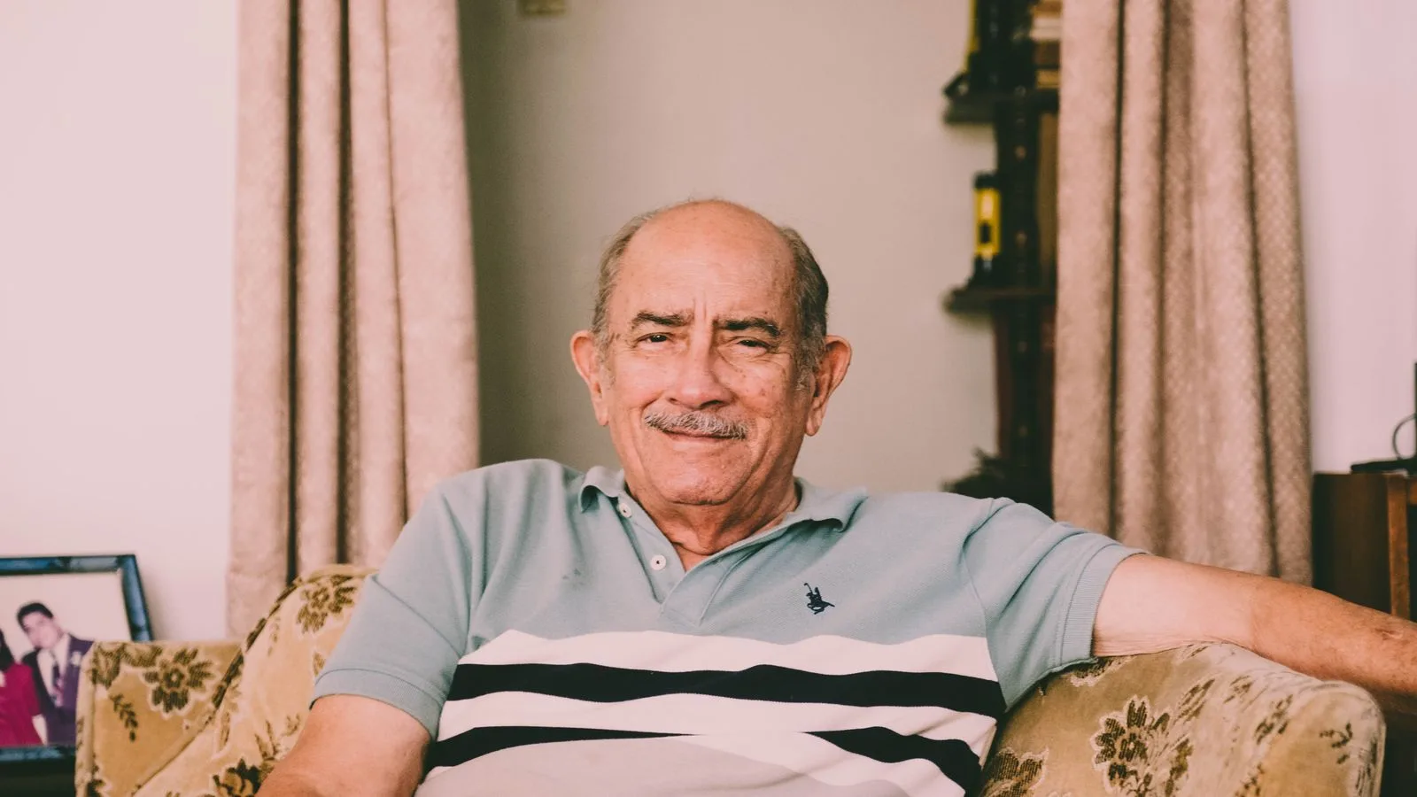 A cheerful elderly man enjoys a relaxed moment on a sofa in a warmly decorated living room.