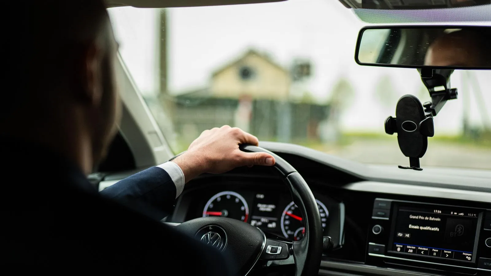 Businessman in suit driving a car, focus on steering wheel and dashboard.