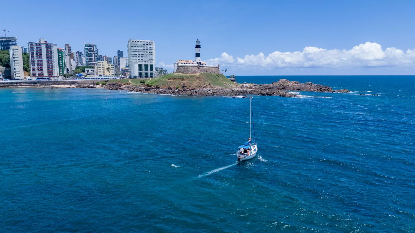 Stunning aerial view of Barra Lighthouse and yacht sailing in Salvador, Brazil's vibrant coast.