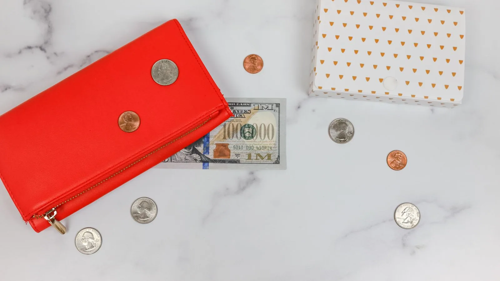 Flat lay of red wallet, US dollars, coins, and gift box on marble surface