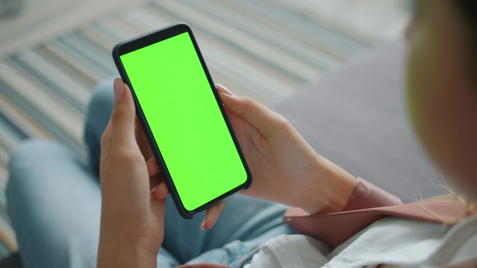 Close-up of a woman holding a smartphone with a green screen for customization.