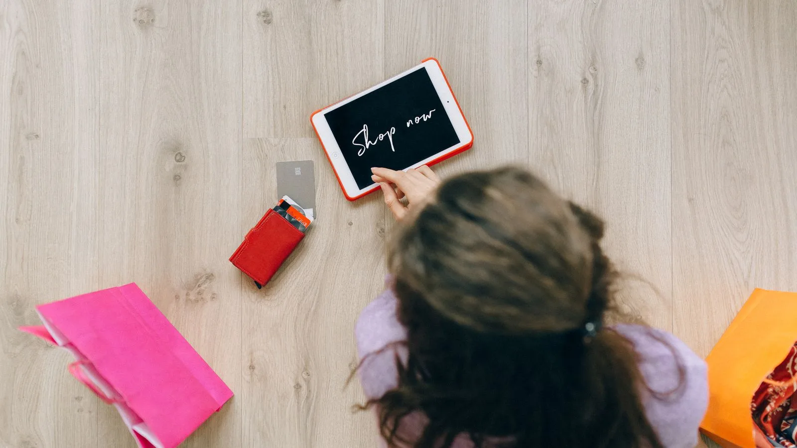 Overhead view of a woman using a tablet for online shopping surrounded by shopping bags and cards.