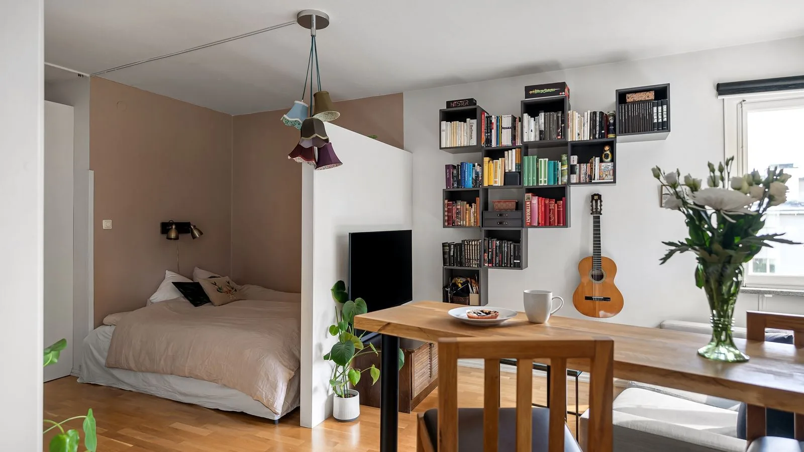 A stylish studio apartment with a cozy bed, bookshelf, and modern decor.