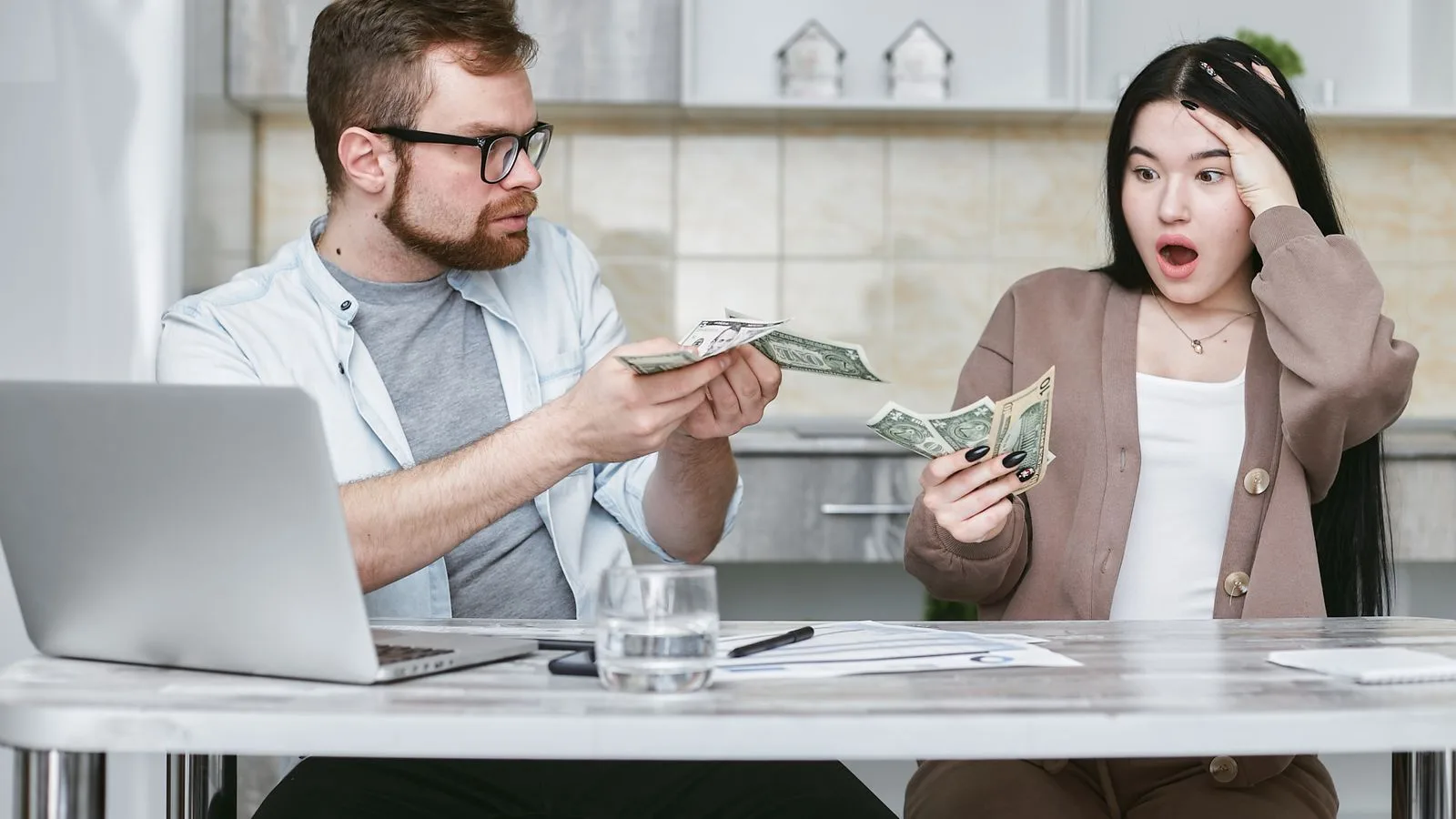 A shocked couple sitting at a table counting cash, illustrating financial surprise.