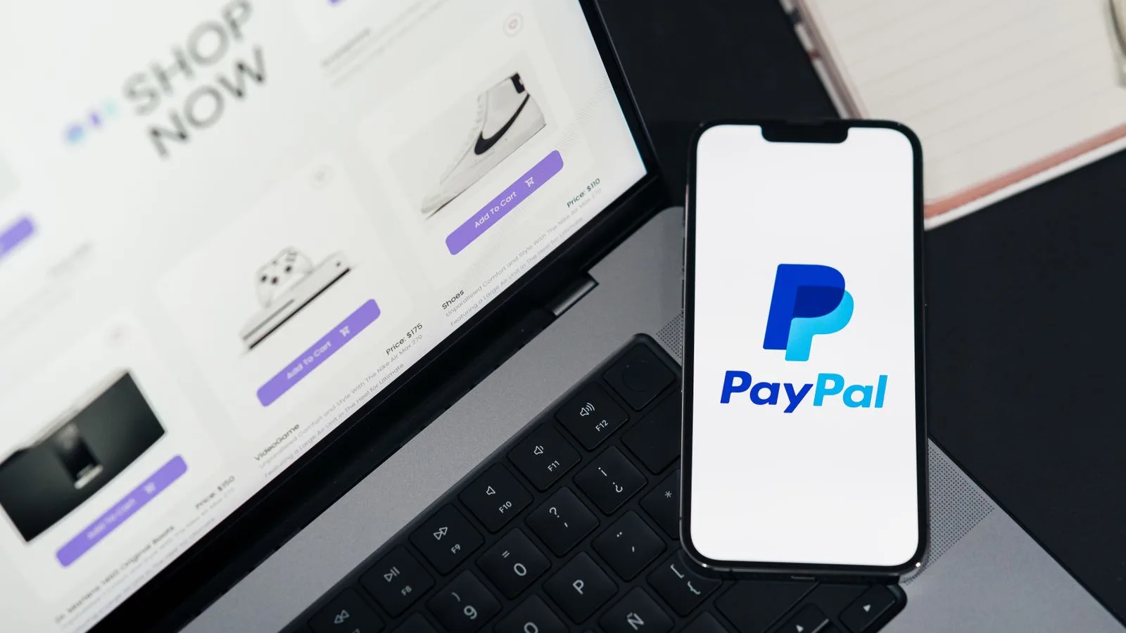 Smartphone displaying PayPal logo next to laptop with online shopping site open.