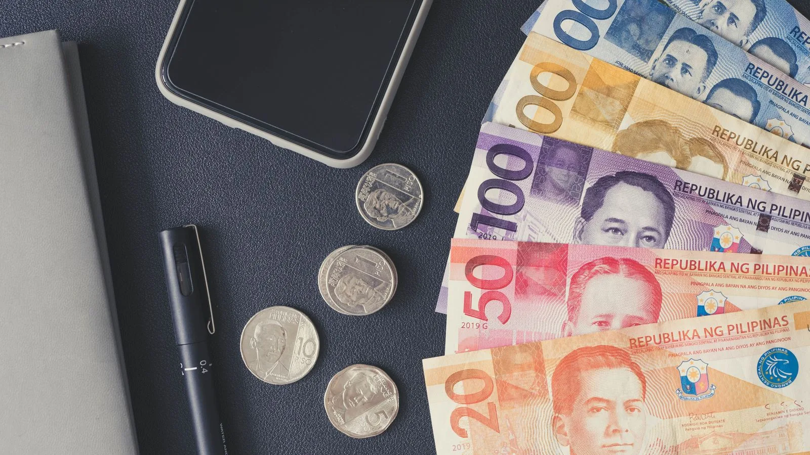 Flat lay of Philippine peso bills, coins, smartphone, and notebook. Ideal for financial themes.