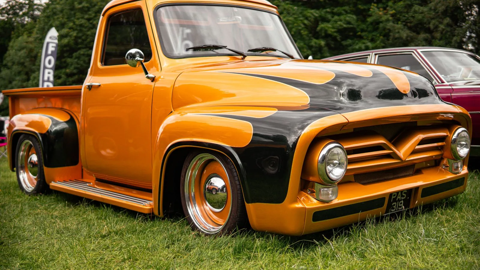 Classic orange Ford pickup truck with custom paint job parked outdoors on green grass.