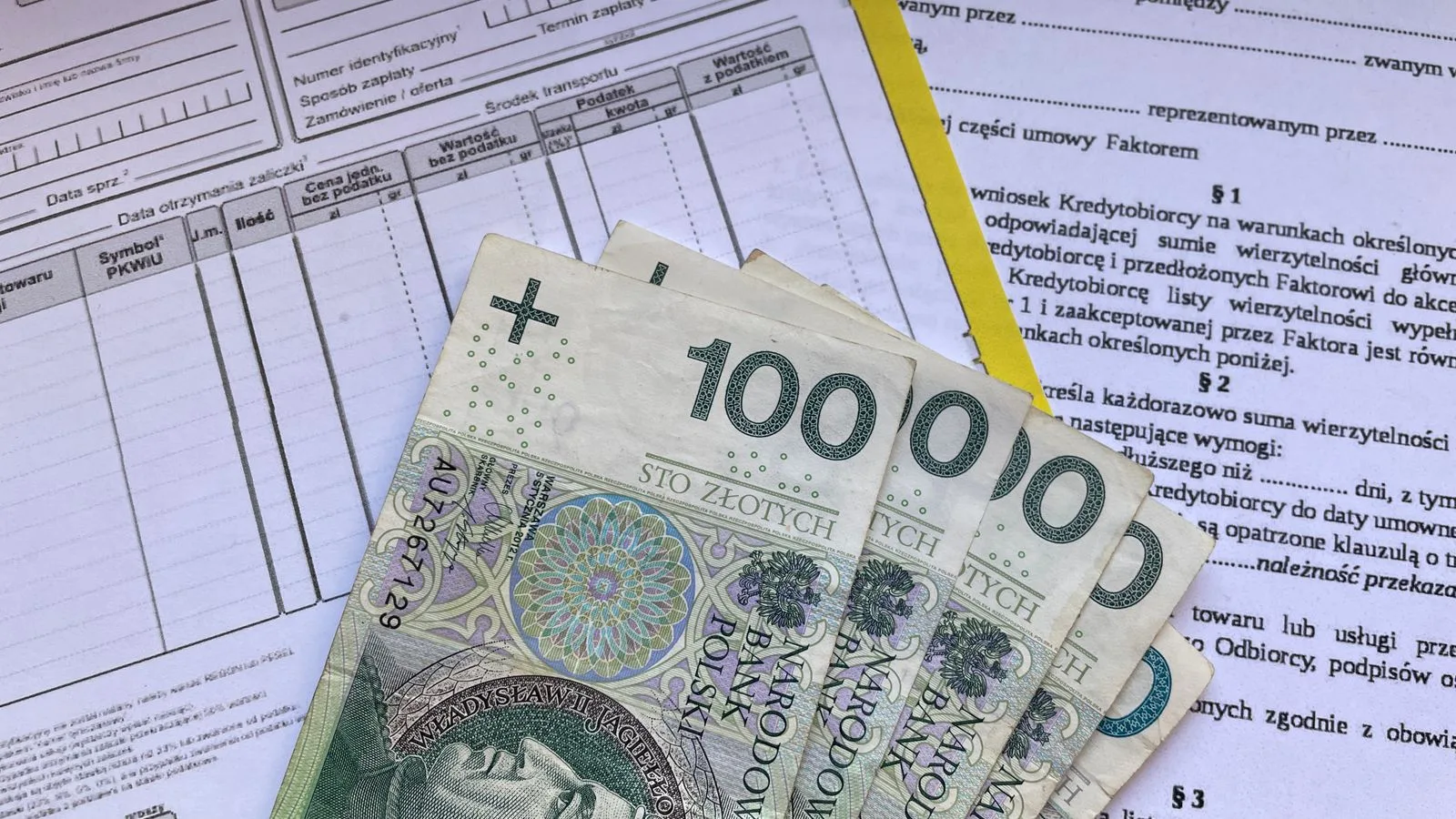 Polish 100 Zloty banknotes on VAT invoice and factoring agreement forms.