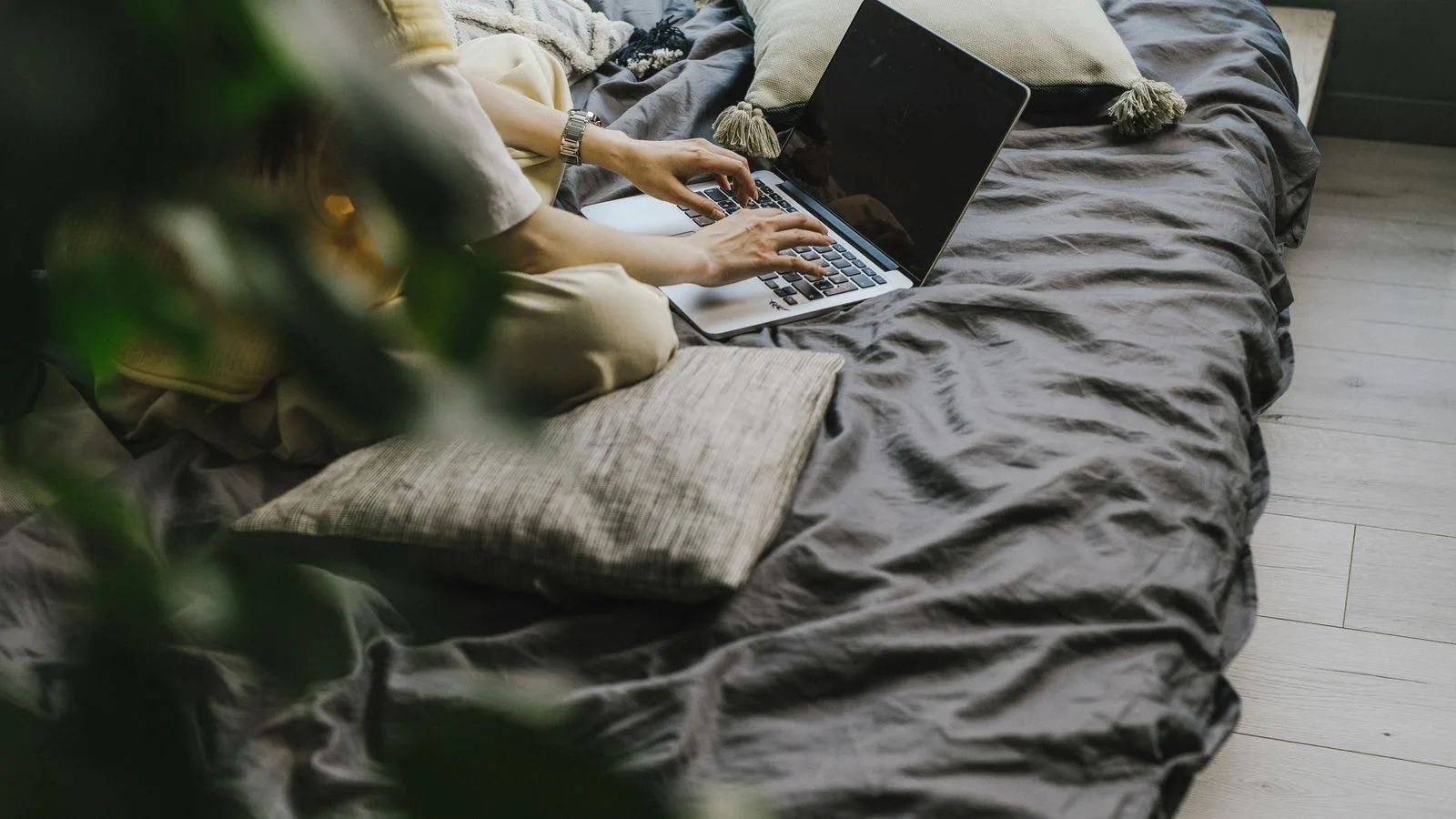 Relaxed work environment with a laptop and person typing on a bed, enjoying comfort while working.