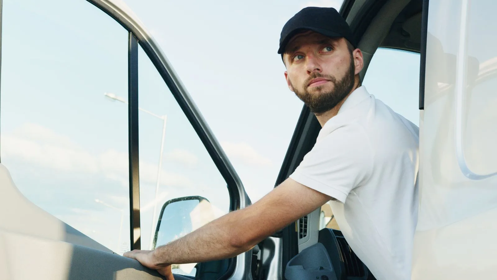 A bearded man wearing a cap enters a van in daylight, showcasing transportation and travel lifestyle.