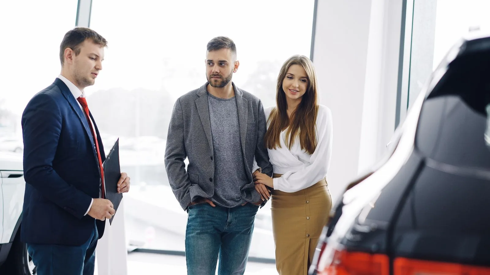 Smiling couple with salesman in car showroom discussing features of a car.