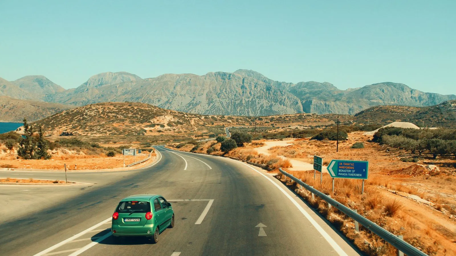 A lone car travels on a winding road through Greece with mountains.