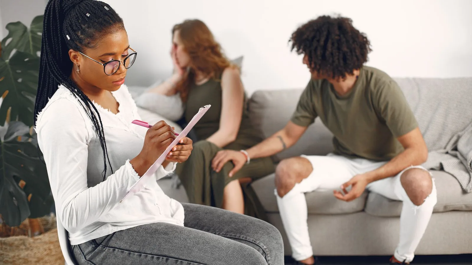 Counseling session with a woman taking notes as a couple discusses in the background.