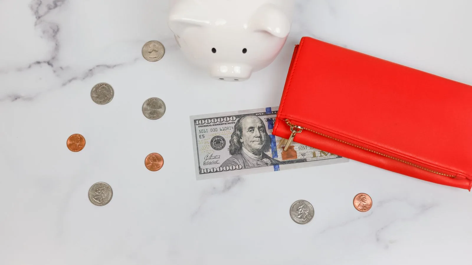 Overhead view of piggy bank, red wallet, and US dollars on marble surface.