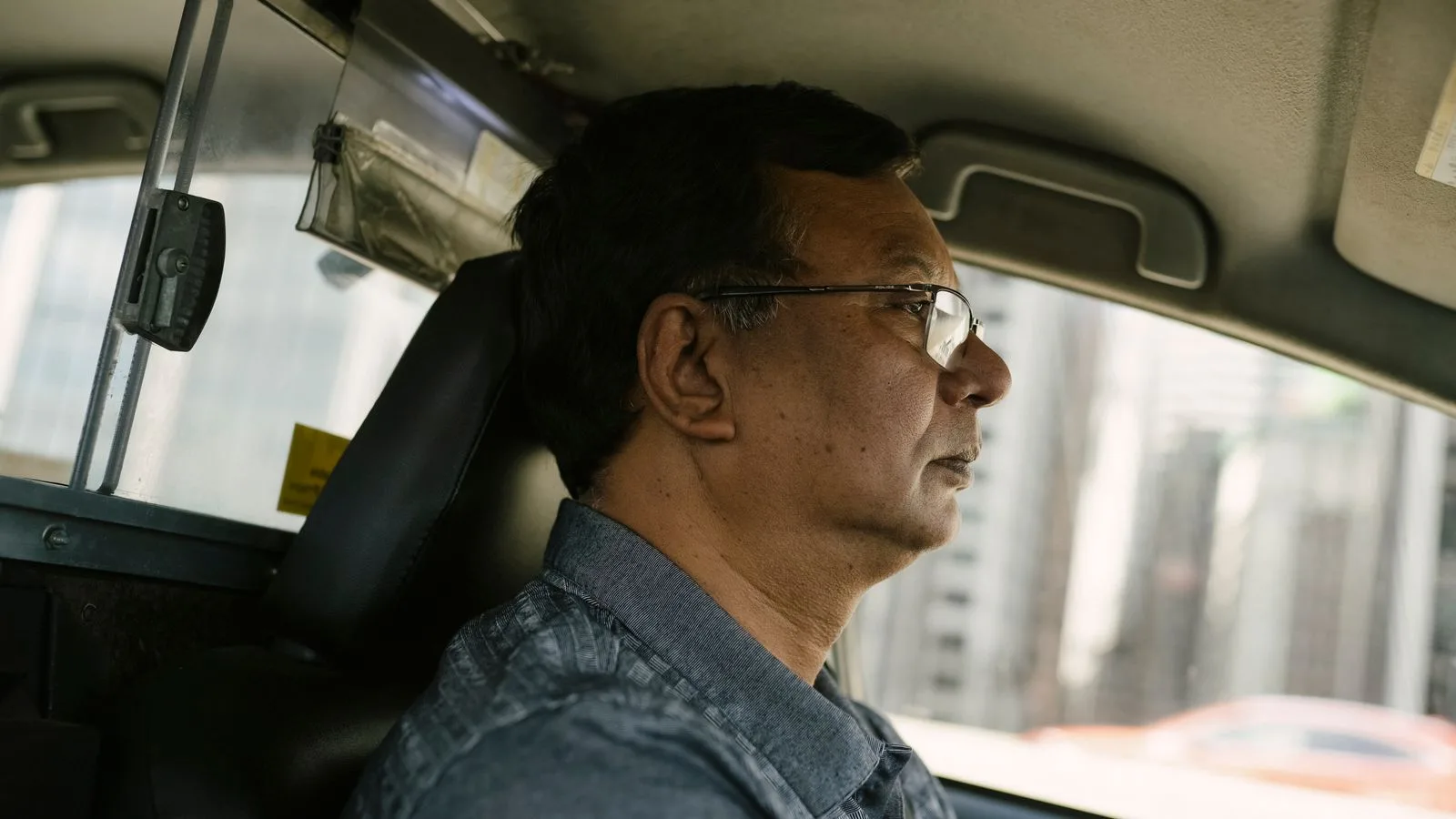 Side view of ethnic male in eyeglasses and casual clothes looking away while driving car