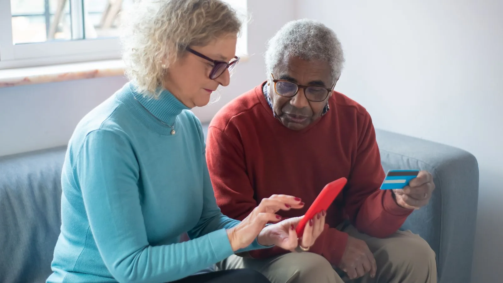 Elderly couple using a smartphone for online shopping, holding a credit card.