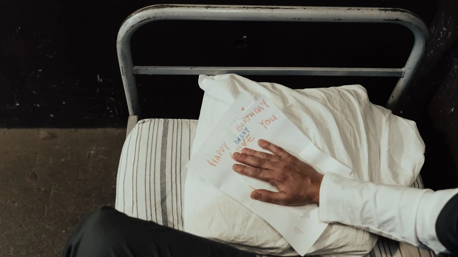 An inmate's hand on a heartfelt birthday card inside a prison cell on a makeshift bed.