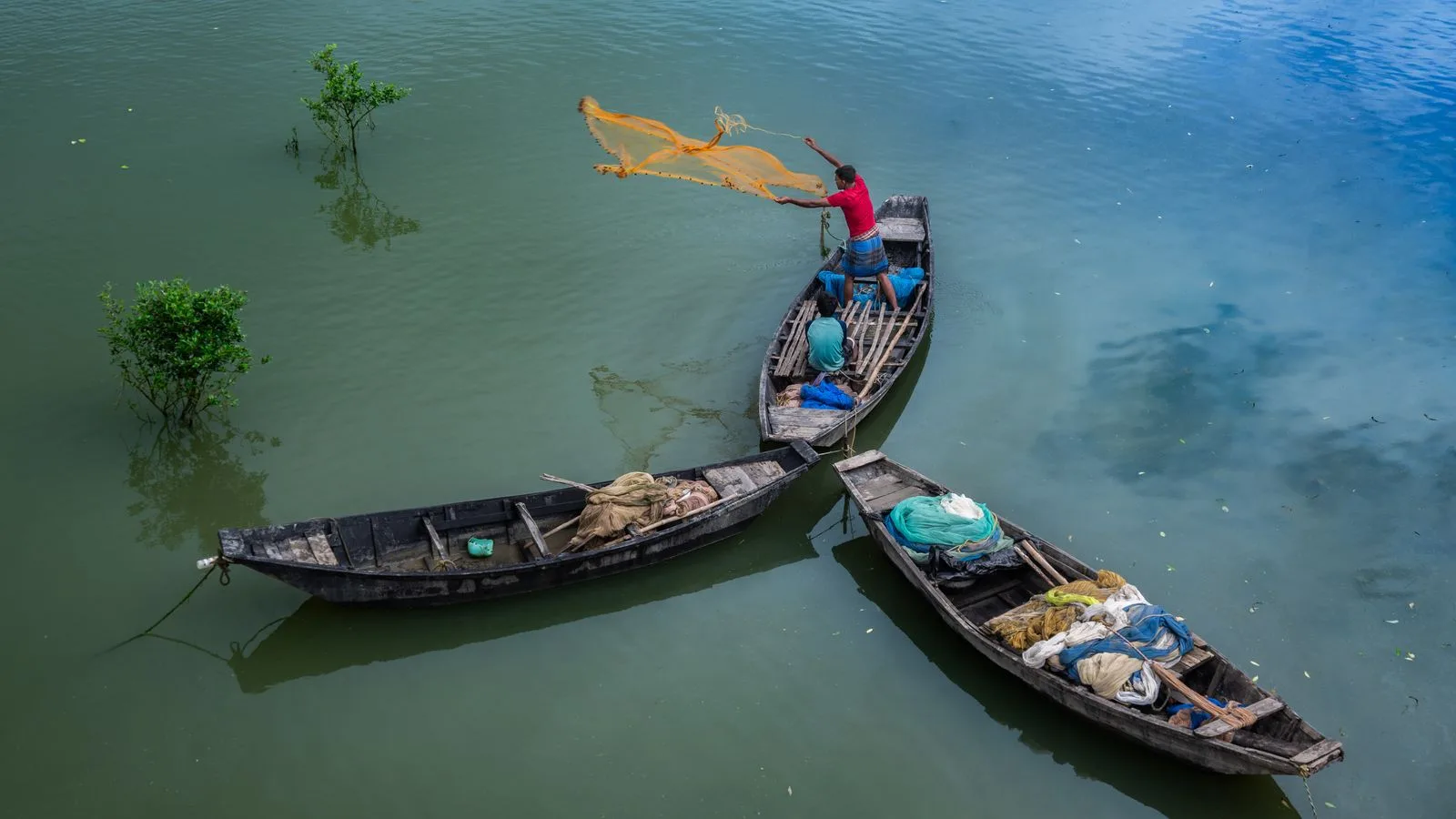 Fishermen casting nets from boats in a serene West Bengal river scene.