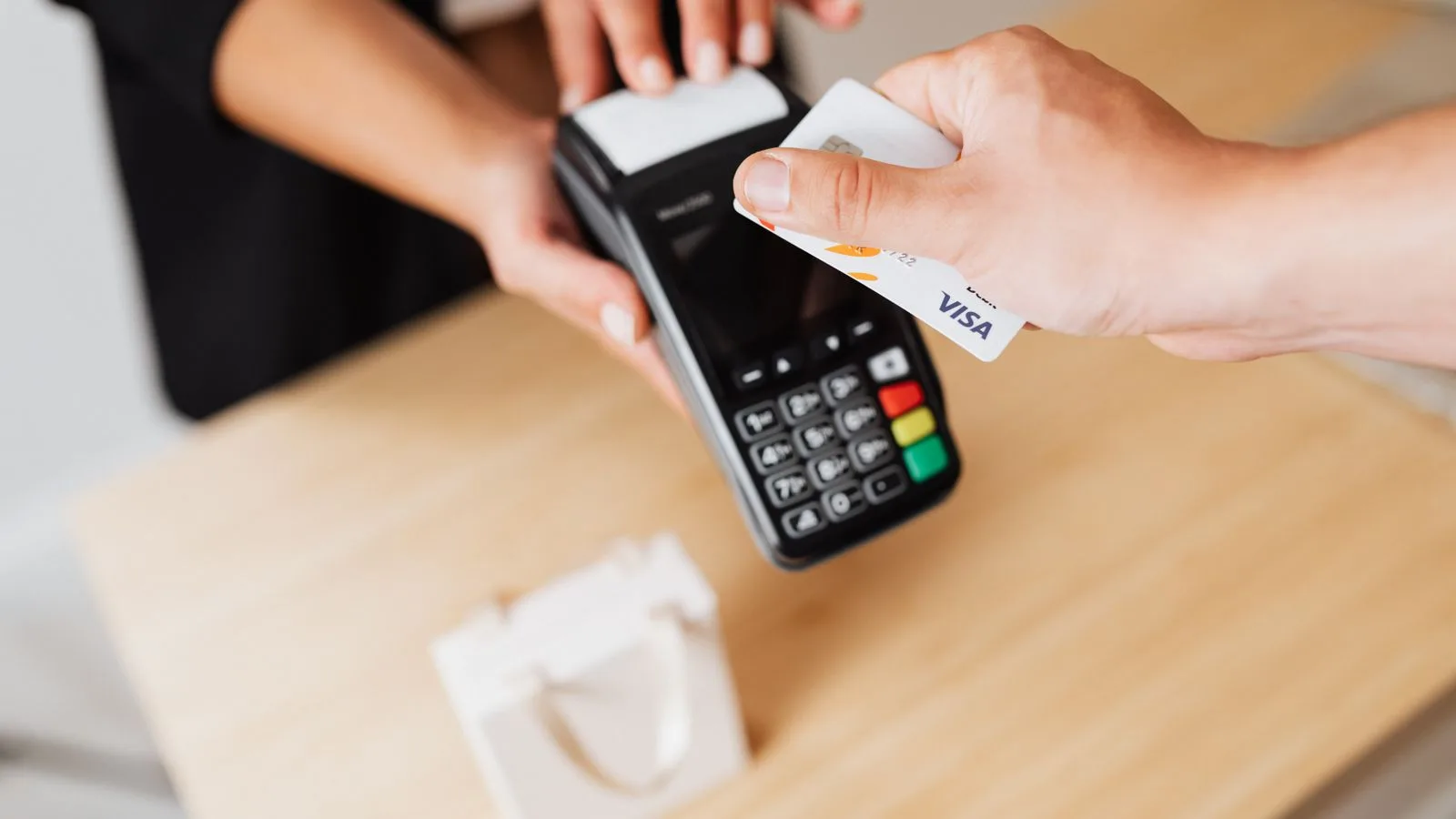 Close-up of hands using a contactless payment terminal with a credit card indoors.