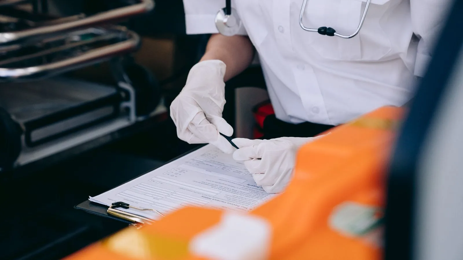 A medic wearing gloves and a stethoscope takes notes inside an ambulance.