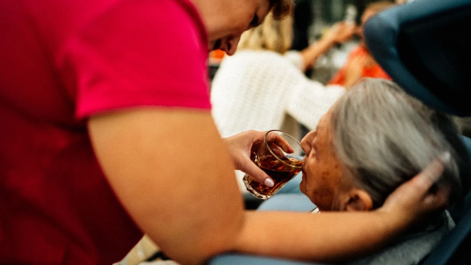 A caregiver helps an elderly woman drink tea, showcasing empathy and support.