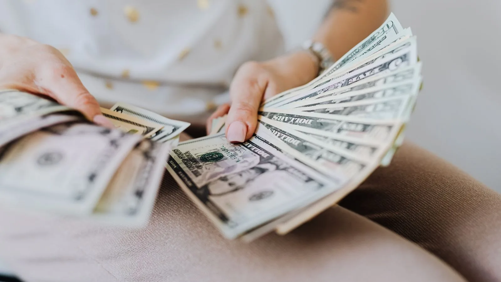 Close-up of hands holding and counting US dollar bills indoors.