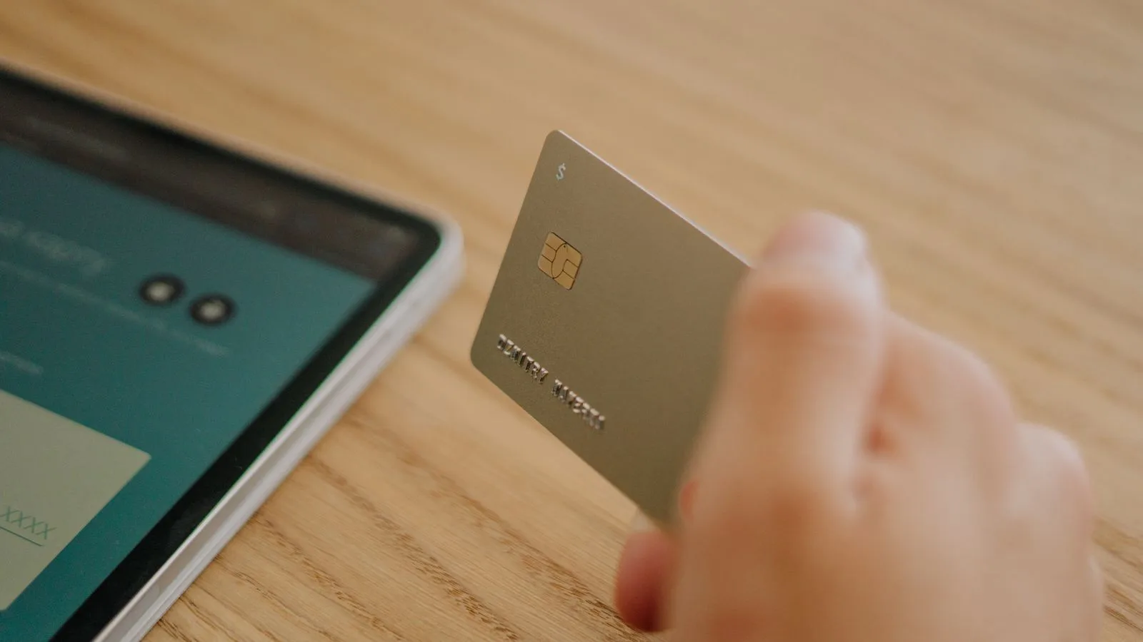 Close-up of a hand holding a credit card near a tablet, depicting online shopping or transaction.