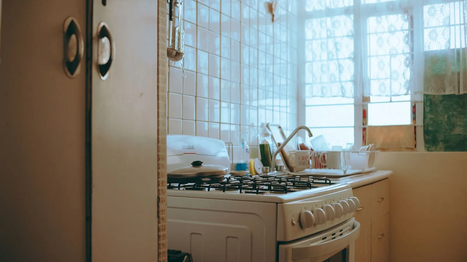 Warm-toned vintage kitchen with stove, tiled walls, and window light creating a homely atmosphere.