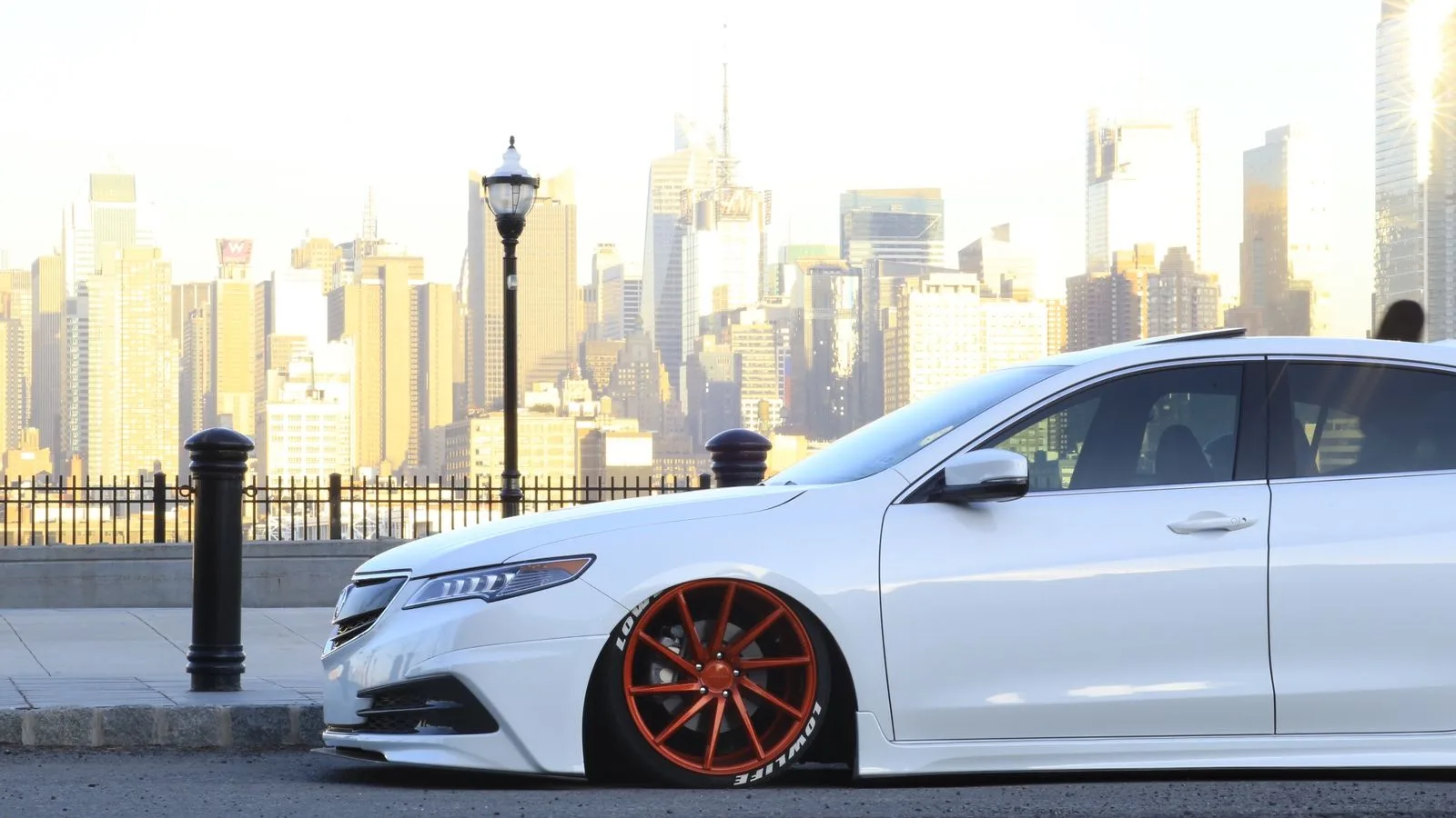 Custom lowered car with vibrant red rims against NYC skyline. Perfect for car enthusiasts.