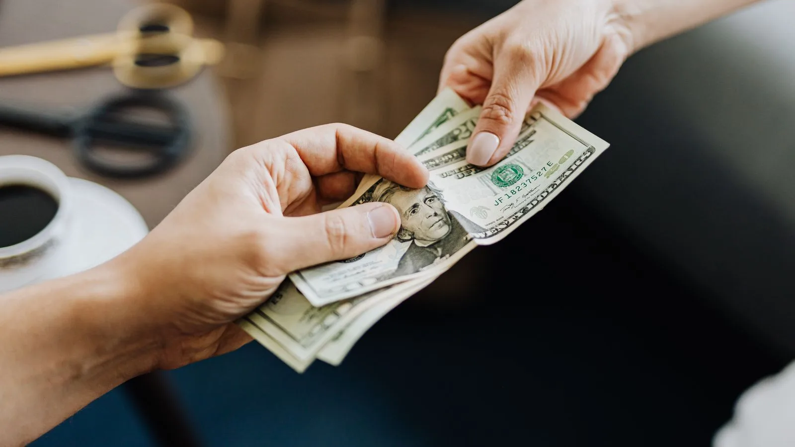 A close-up image of hands exchanging US dollar bills, symbolizing financial transaction or payment.