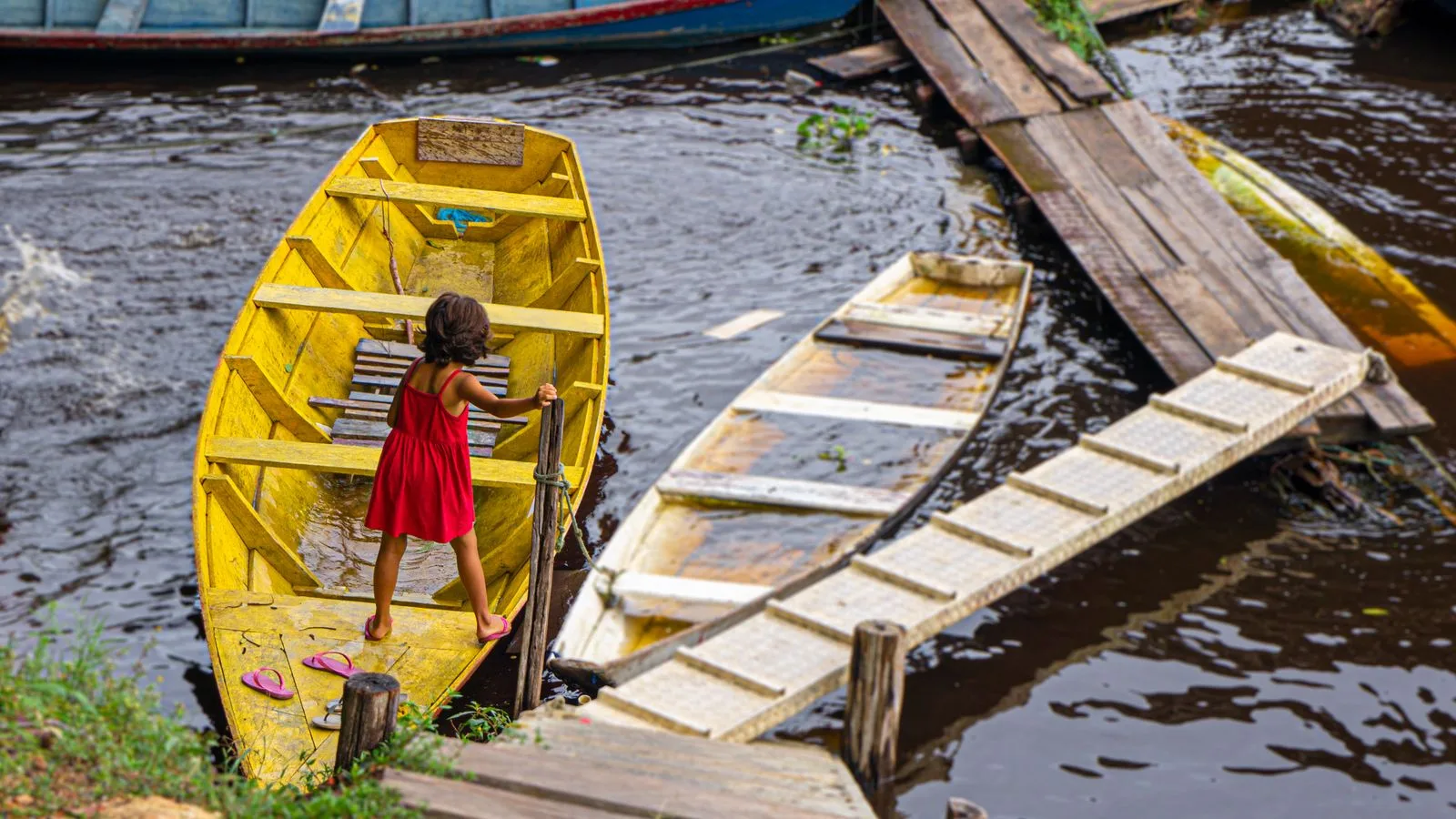 Young girl in red dress navigating a yellow boat on a river in Manaus, Brazil.