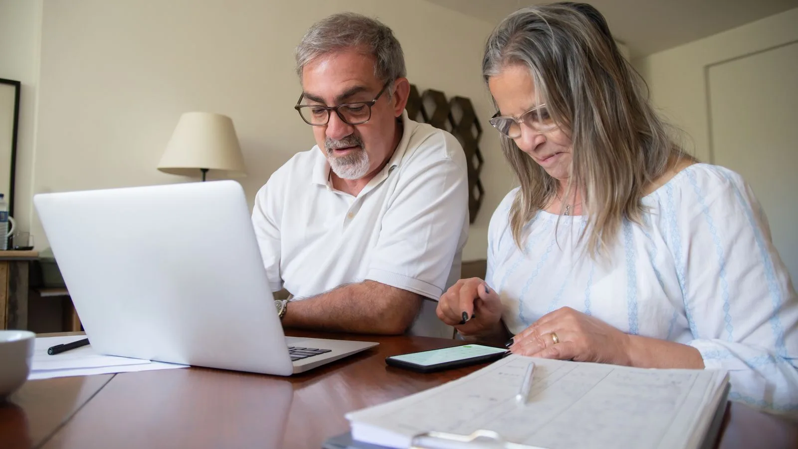 Senior couple working together on documents with laptop and phone at home.