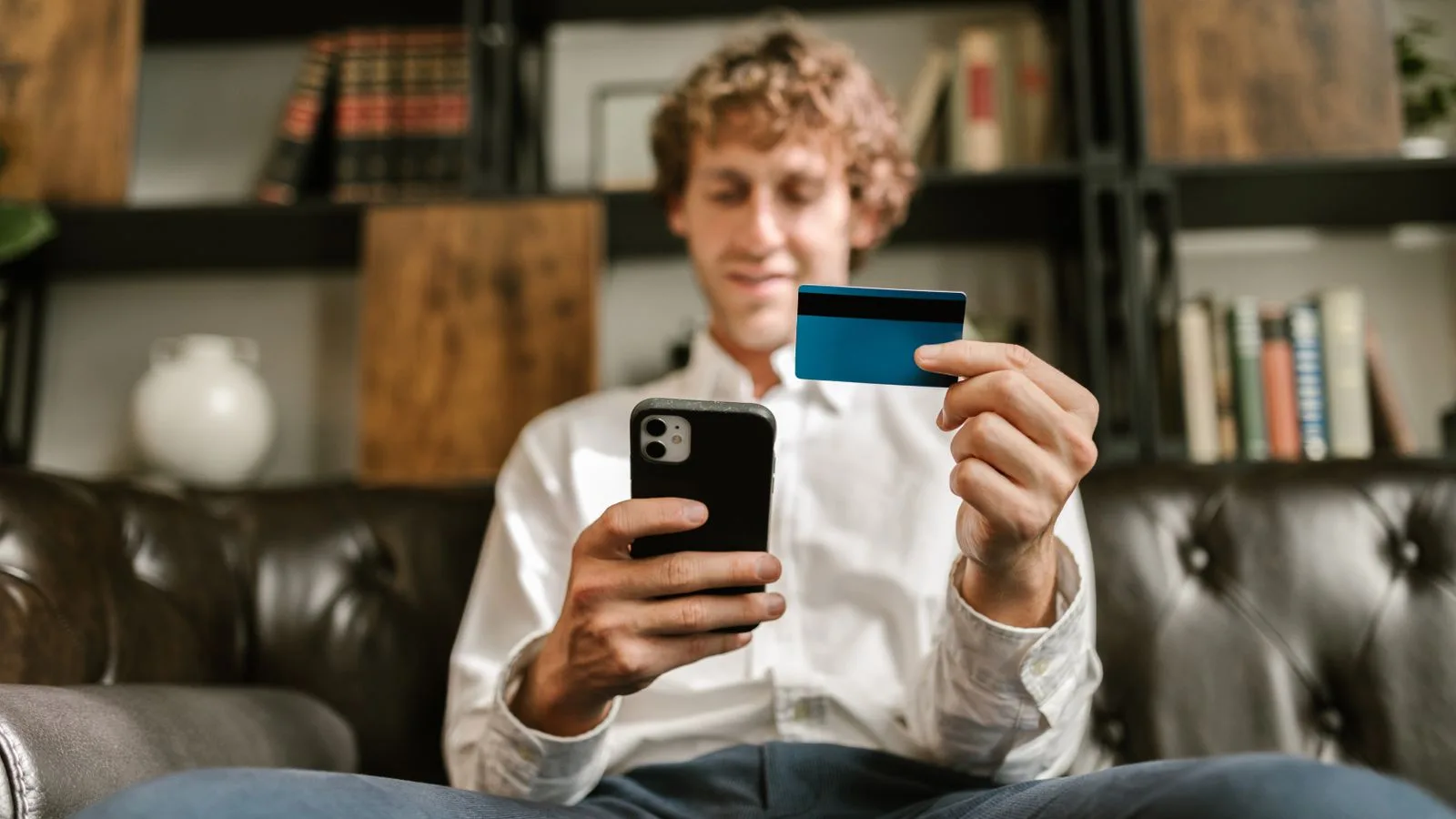 A man smiles while using his smartphone and credit card for online shopping.