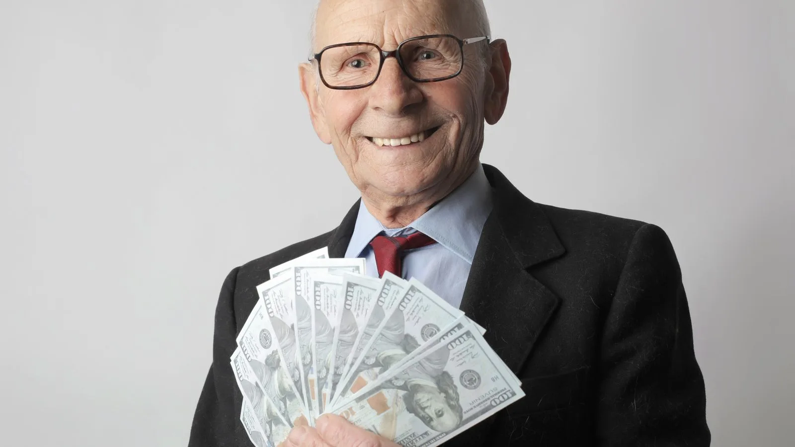 Senior man in a suit with glasses holding US dollars, symbolizing wealth and savings.