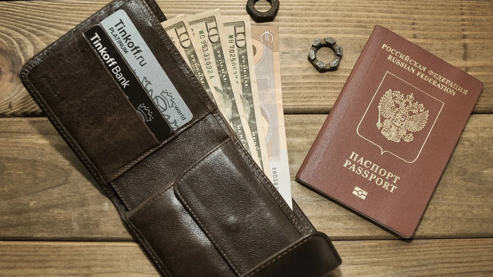 Brown leather wallet with cards, assorted currencies, and passport on wood surface.