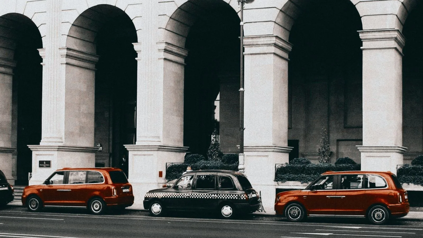 A vintage scene of taxis parked against grand architectural arches.