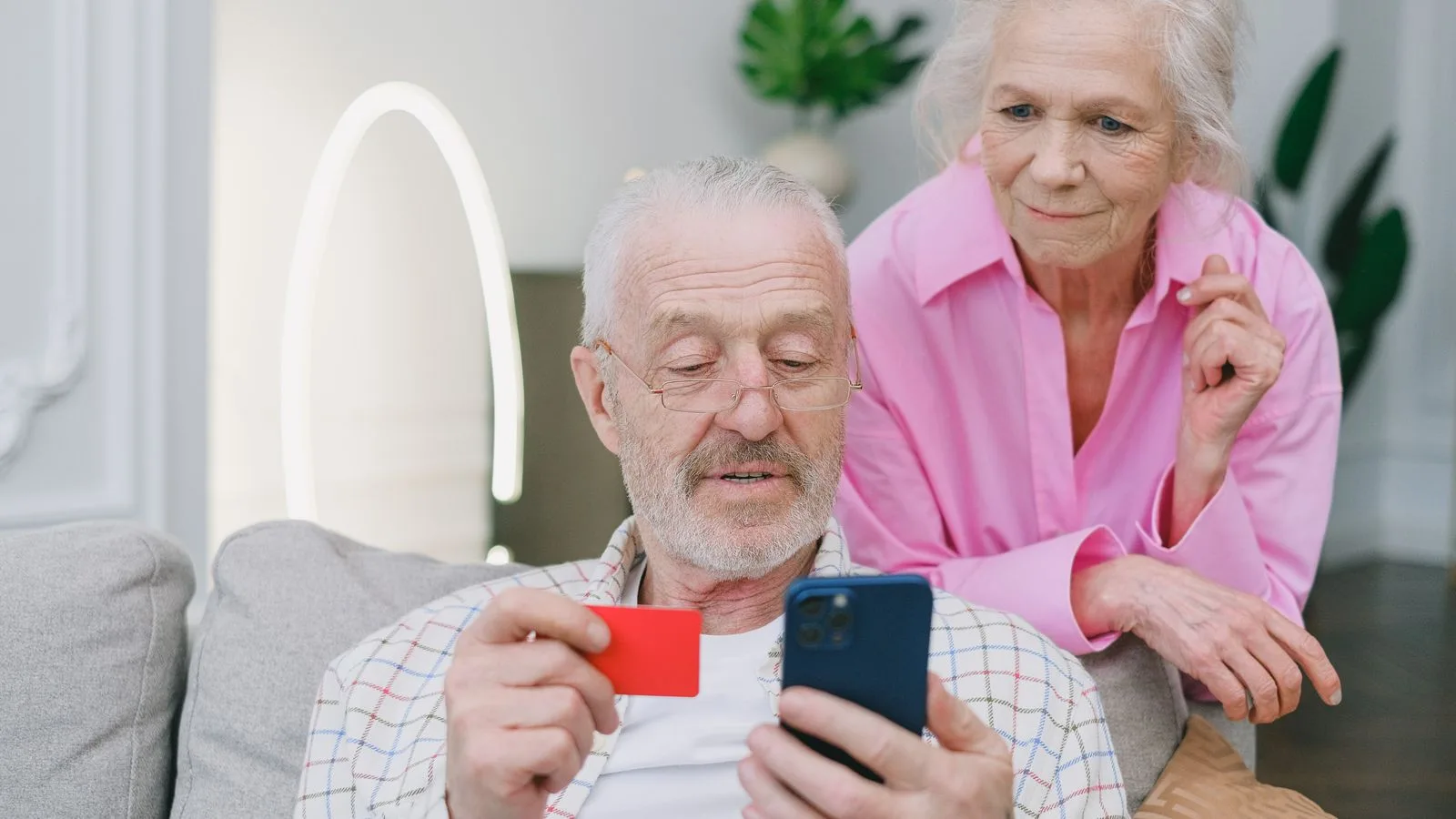 Elderly couple using smartphone and credit card for online shopping at home.