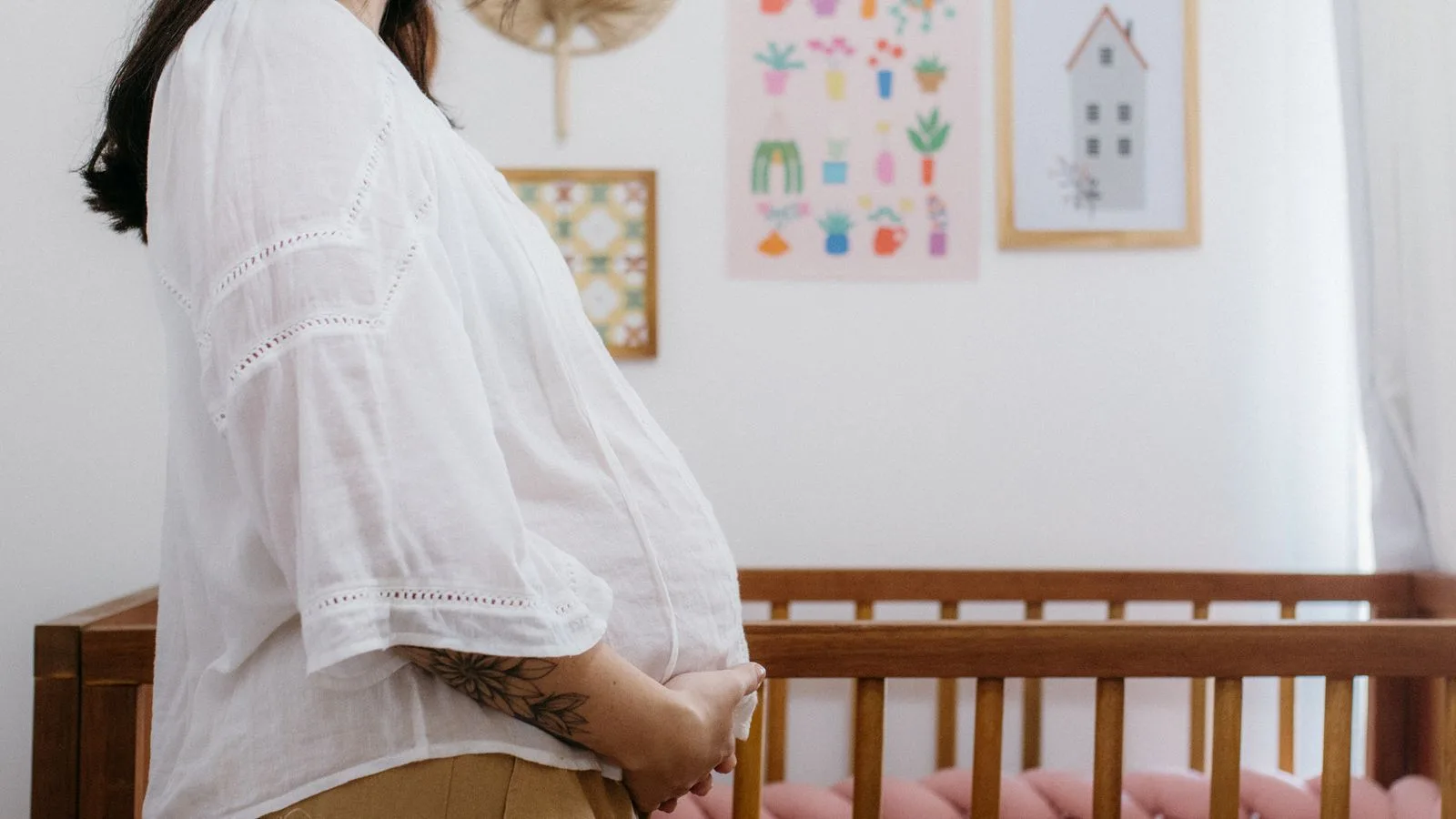 Expectant mother standing beside a wooden crib in a beautifully decorated nursery room.